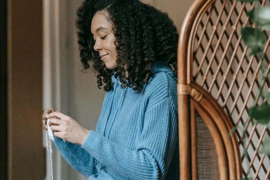 A Woman in Knitted Sweater Sitting while Holding a Yarn