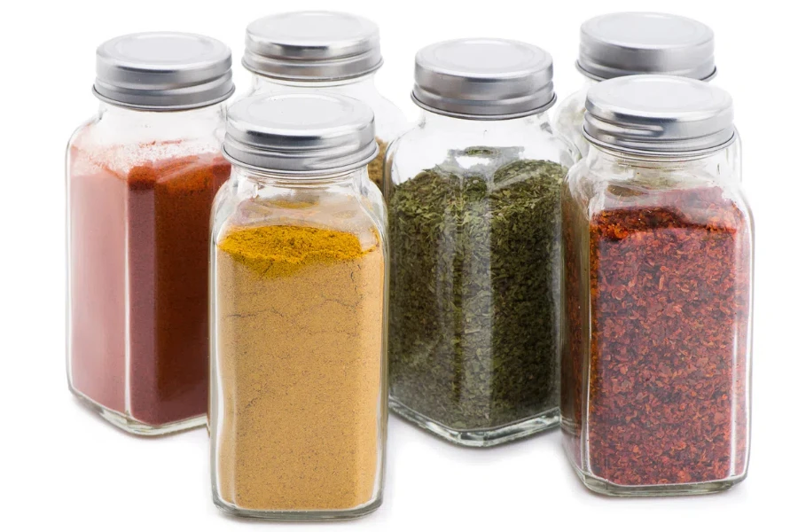 A group of seasonings in glass jars on a light stone background with shadows