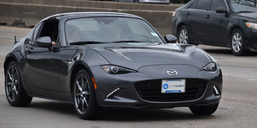 A portrait of a black Mazda MX-5 sports car traveling down a highway in moderate traffic