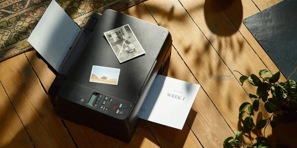 A printer on a wooden floor next to a flower vase
