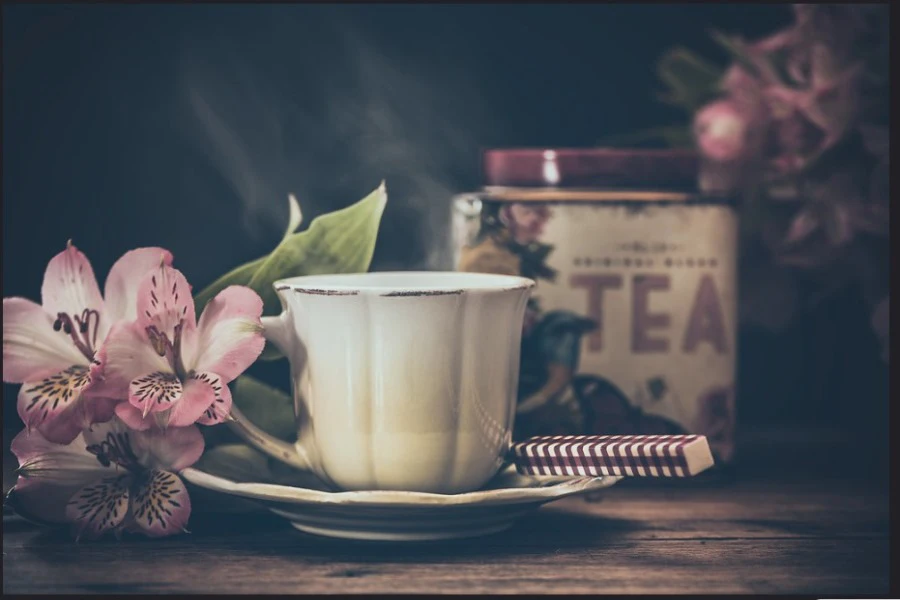 A white teacup with flower and tea tin in the background