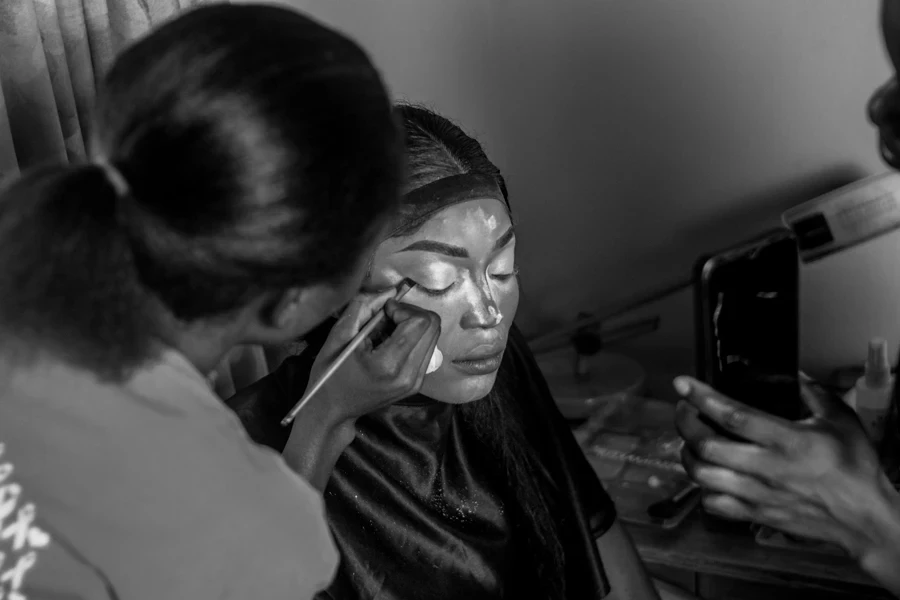 A woman is getting her makeup done by another woman