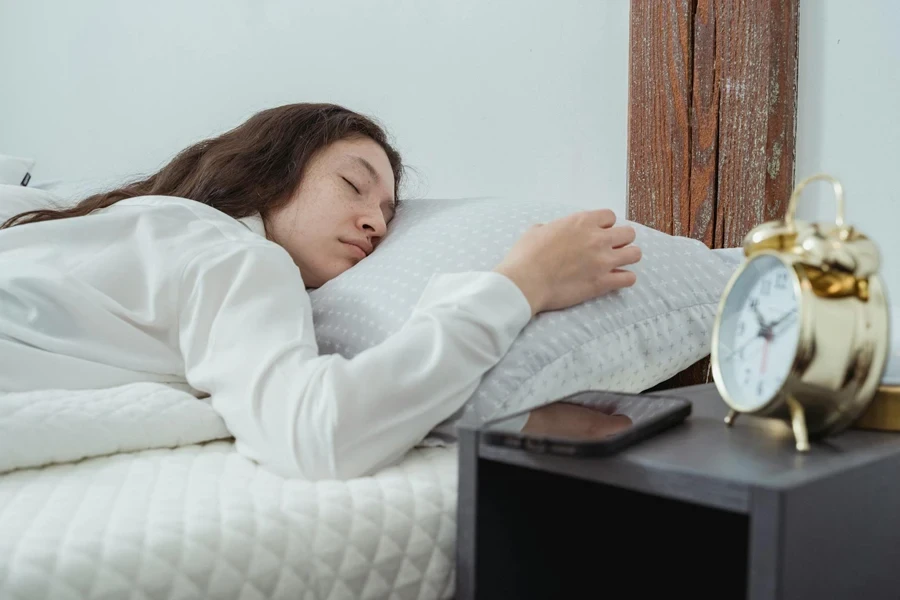 A woman sleeping peacefully on a bed bedside table with alarm clock and smartphone 