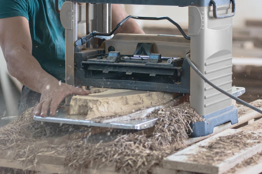 A young adult man processes pieces of walnut wood using a portable bench planer