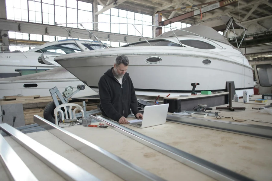Adult worker using laptop at workbench during work in boat garage 