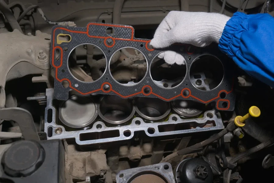 An auto mechanic holds a gasket over a car engine block with his hand