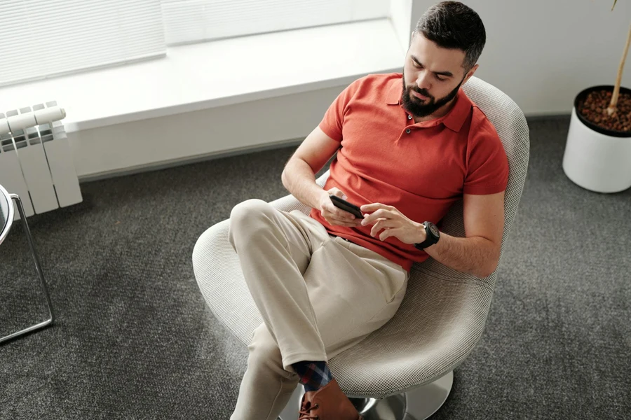 Bearded Man Sitting on Chair While Using a Cellphone