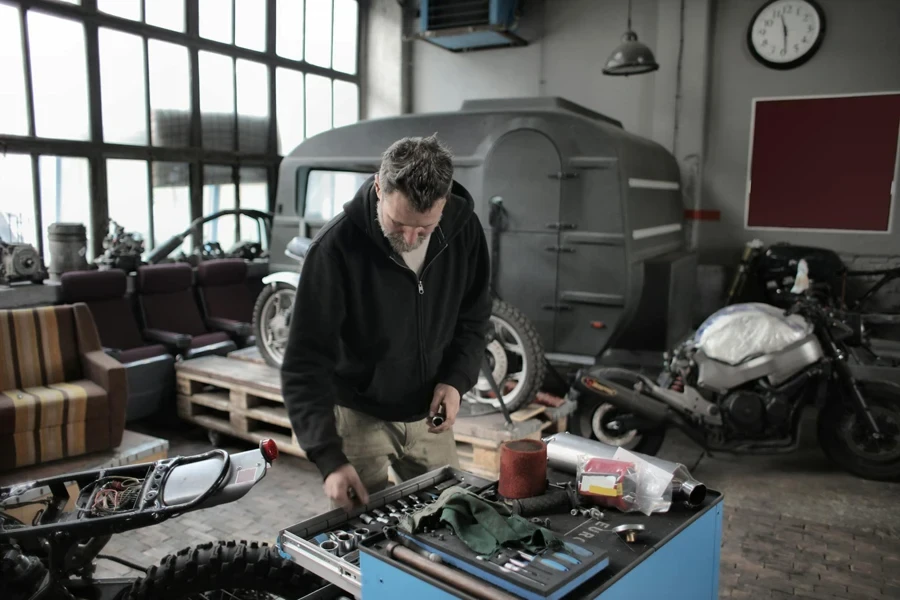 Bearded adult mechanic in casual clothes checking tools while working with vehicle in workshop 