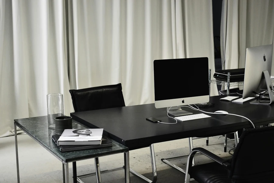 Black and white of workspace of office with computers placed on table with wireless mouse and keyboard near smartphone