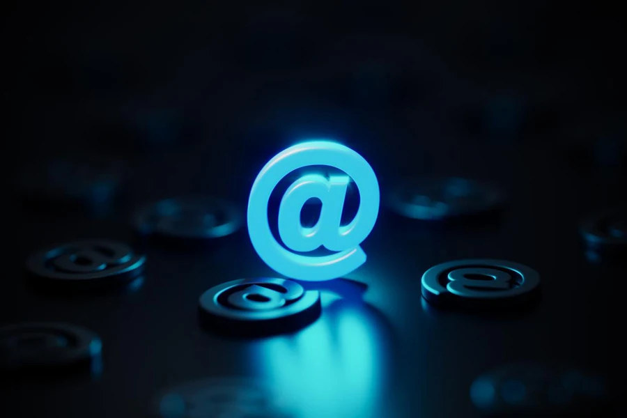 Blue at symbol glowing amid black at symbols on black background. Communication and e-mail concept.