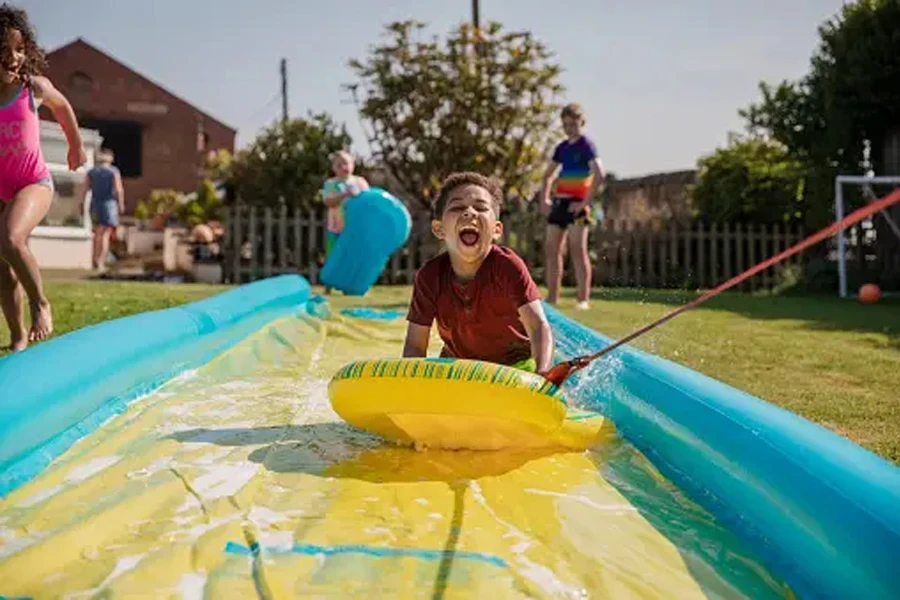 Children playing outside in a garden in the North East of England on a slip and slide. They are laughing and having fun and a boy is being pulled down the slide.