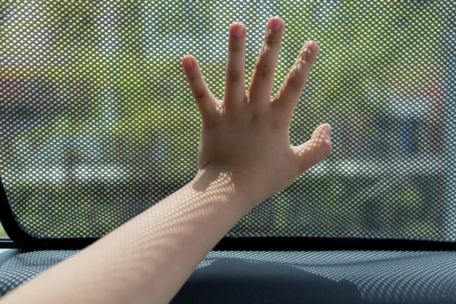 Close up kid hand touching fabric made sunshade in the car side window