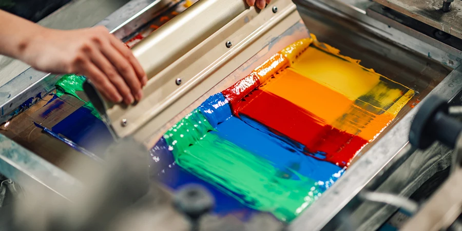 Close up of graphic technician's hands pressing ink into silk and screen printing with squeegee at printing shop