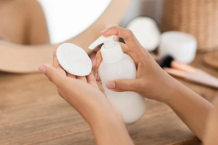 Closeup of female hands holding cotton pad and bottle with toner or cleansing milk