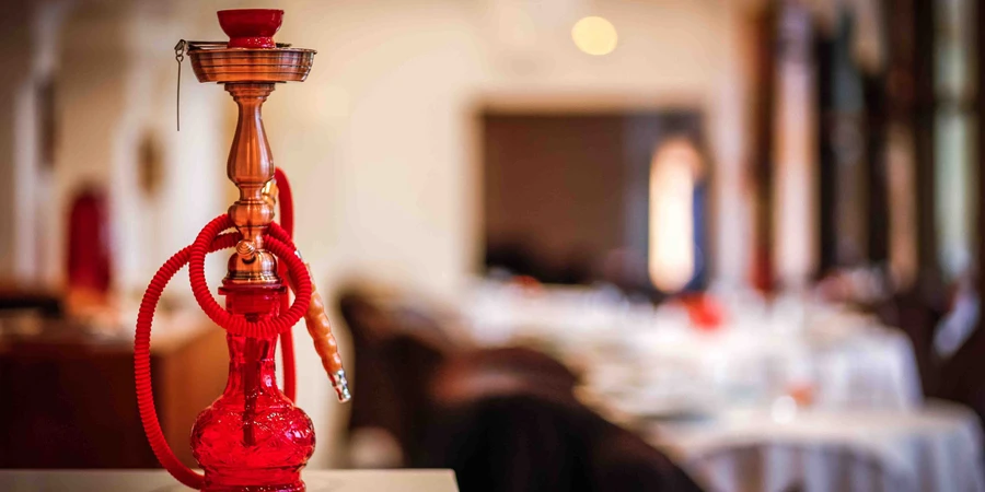 Closeup of the red hookah with glass flask on wooden surface in cafe