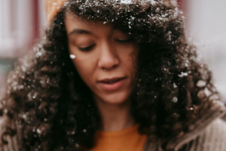 Concentrated African American female with snowflakes on curly dark hair wearing yellow sweater
