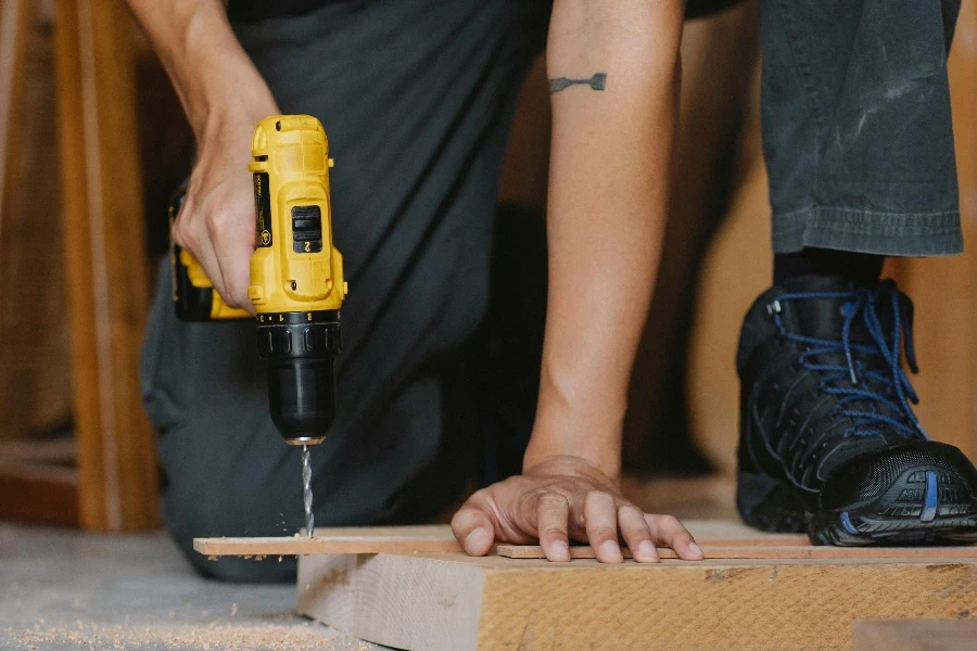 male drilling and pressing timber detail with foot in boot in workshop