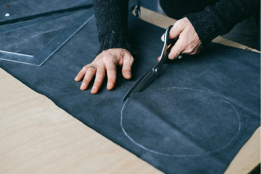 crop male artisan cutting piece of fabric at workbench