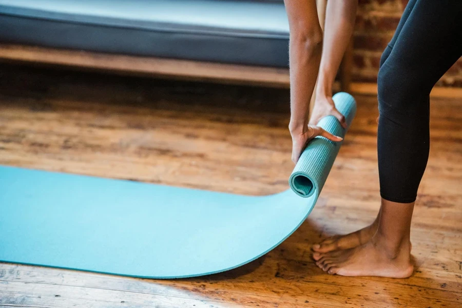 Crop unrecognizable ethnic woman in leggings preparing yoga mat for training in studio in daytime 