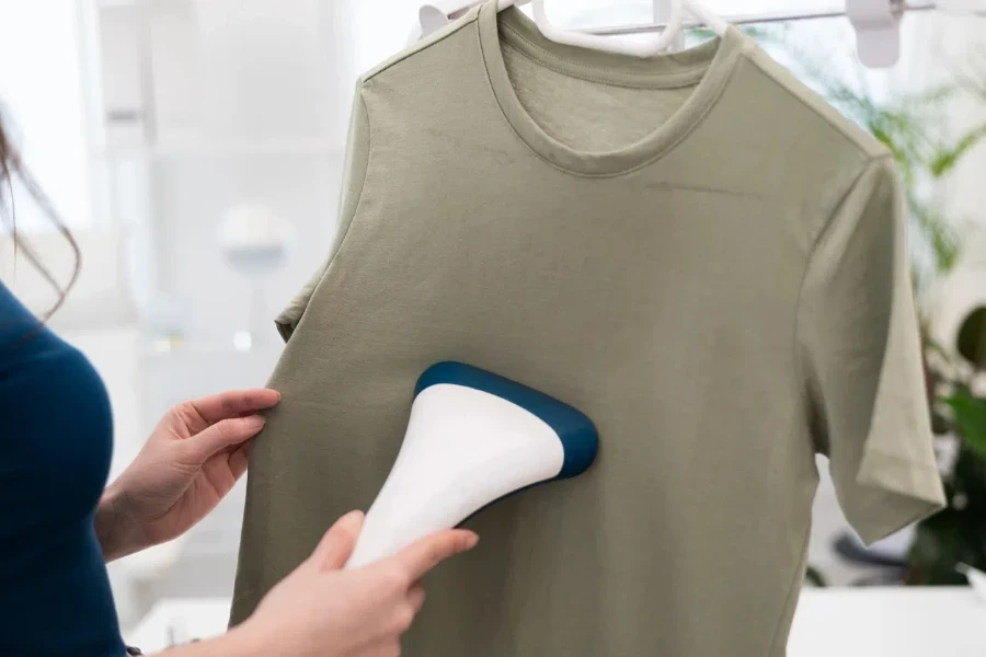 Cropped woman using steaming iron to ironing fashion shirt at home in bright cozy room