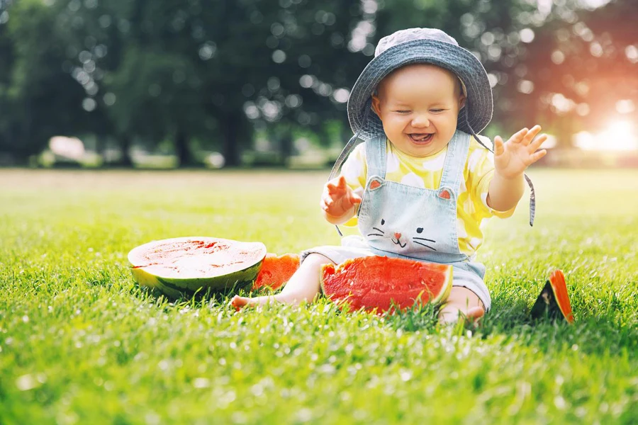 Cutest smiling baby girl eating watermelon on green grass in summertime