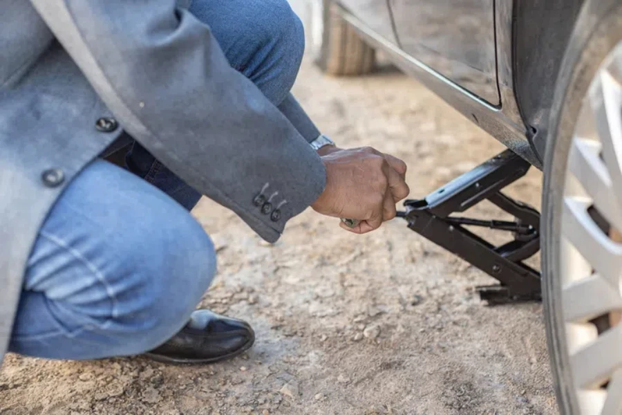 Detail of a latino man changing a flat tire on his car at the side of the road