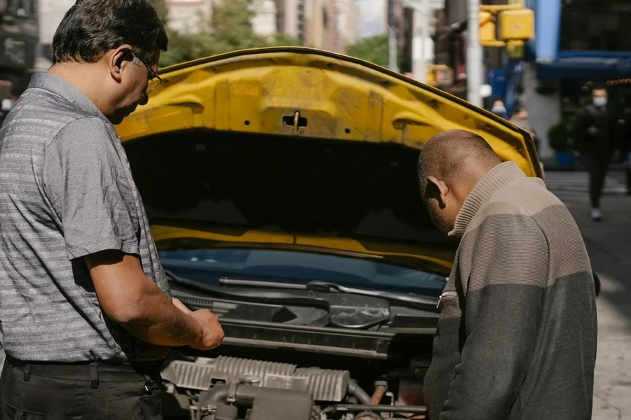 Ethnic mechanic checking car standing near man