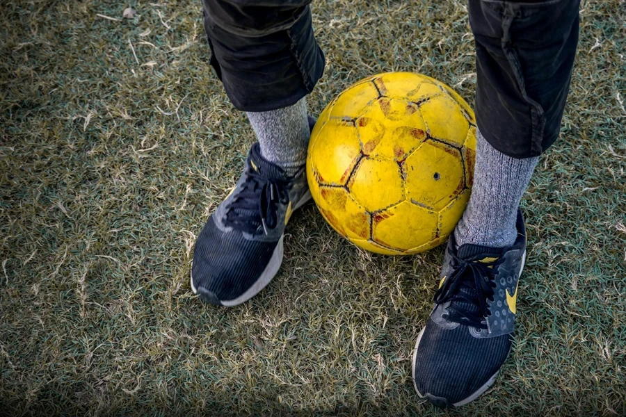 Faceless person standing with soccer ball between legs on grass