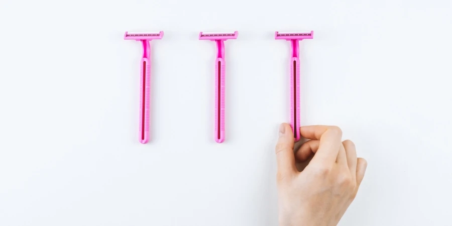 Female hand takes pink disposable razor for hair removal isolated on white background