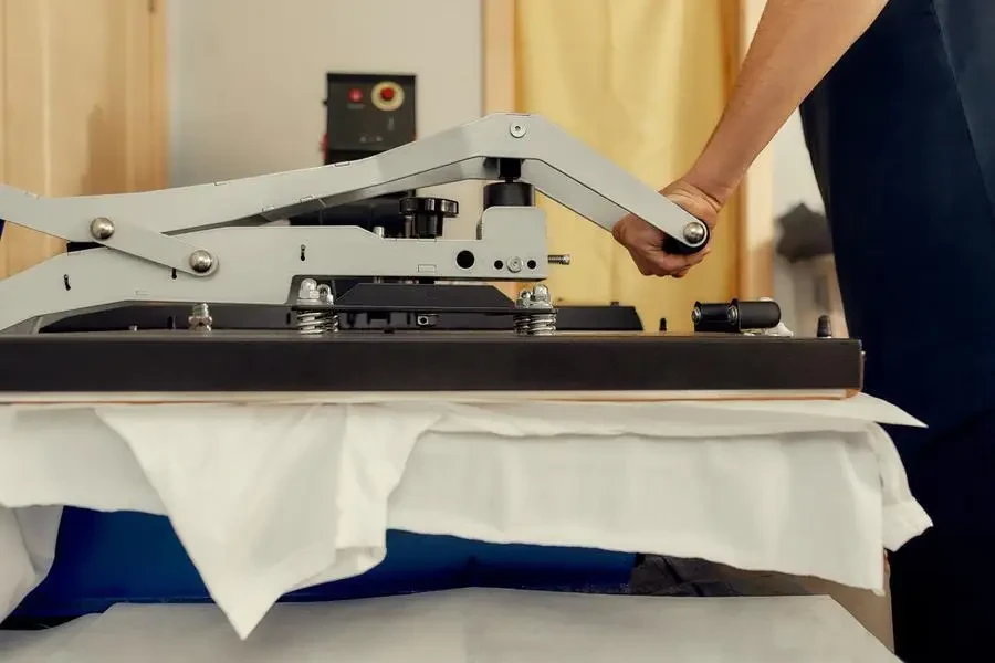 For all printing solutions. Cropped shot of male worker using heat press transfer machine for printing t-shirt stock photo