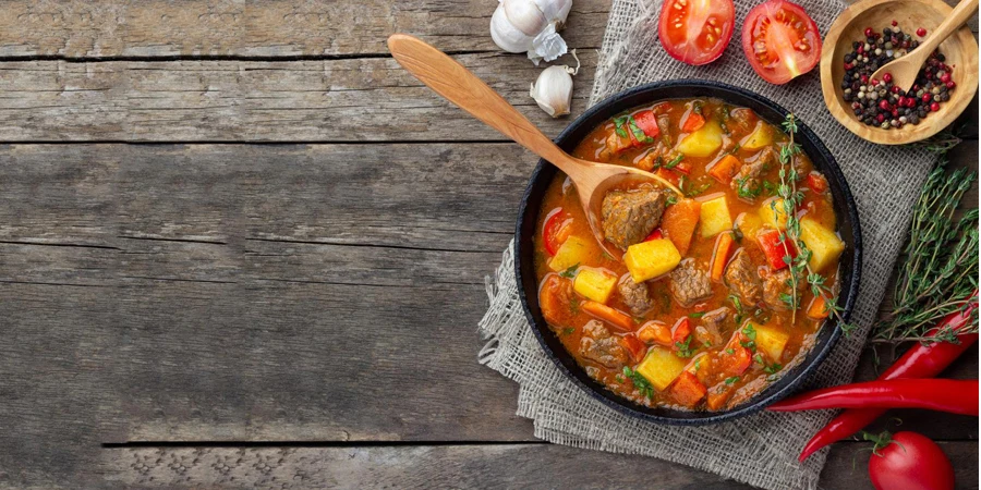 Goulash, beef stew or bogrash soup with meat, vegetables and spices in cast iron pan