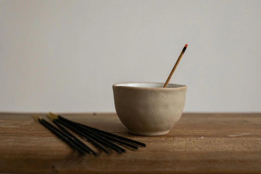 Incense sticks kept next to a diffuser holding one lit incense stick on a wooden table