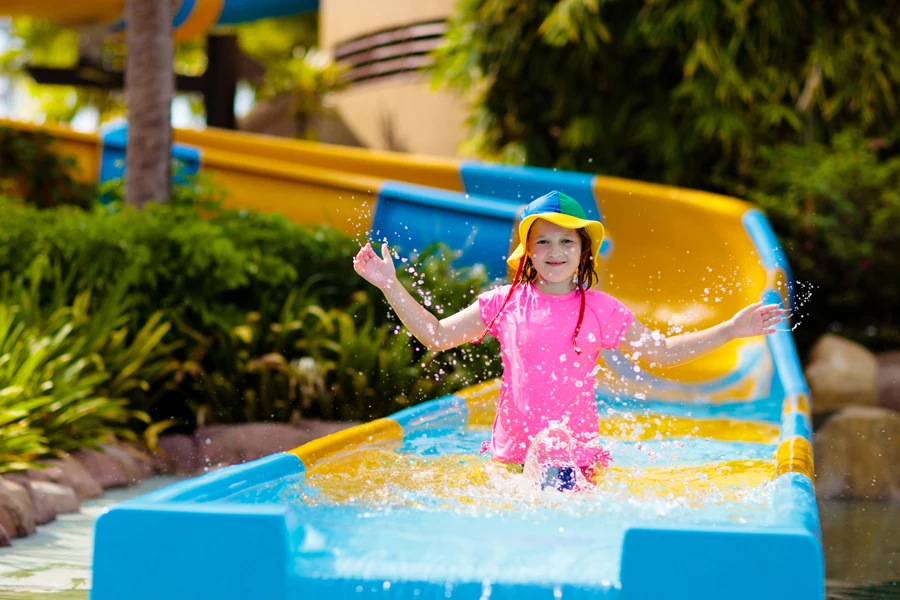 Kids on water slide in aqua park. Children having fun on water slides on family summer vacation in tropical resort. Amusement park with wet playground for young child and baby.