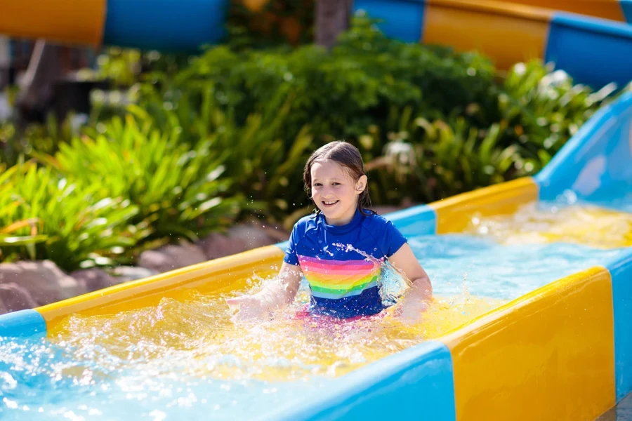 Kids on water slide in aqua park. Children having fun on water slides on family summer vacation in tropical resort. Amusement park with wet playground for young child and baby