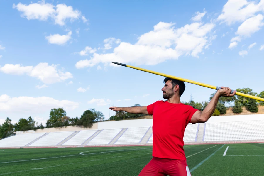 Male athlete in red sportswear throwing tailwind javelin