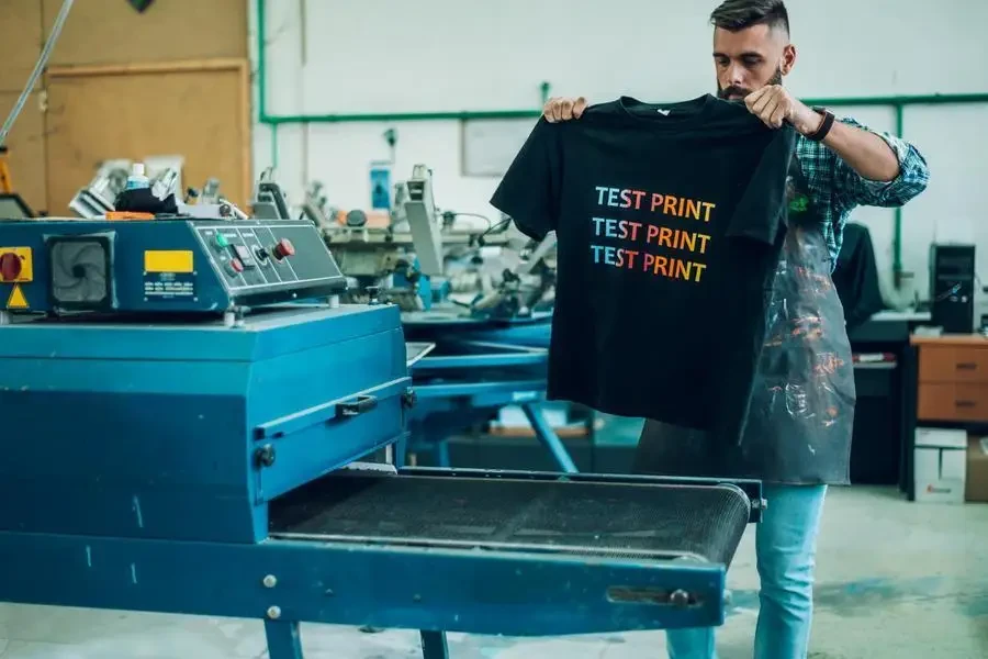 Male worker using a drying oven for t-shirt in a workshop stock photo