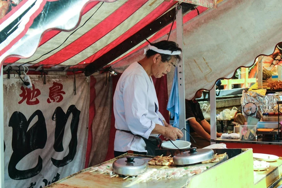 Hombre con bata blanca cocinando en un puesto del mercado