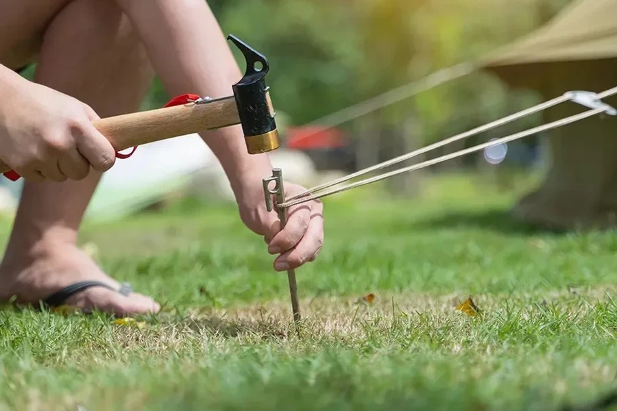 Man setting tent peg with a hammer