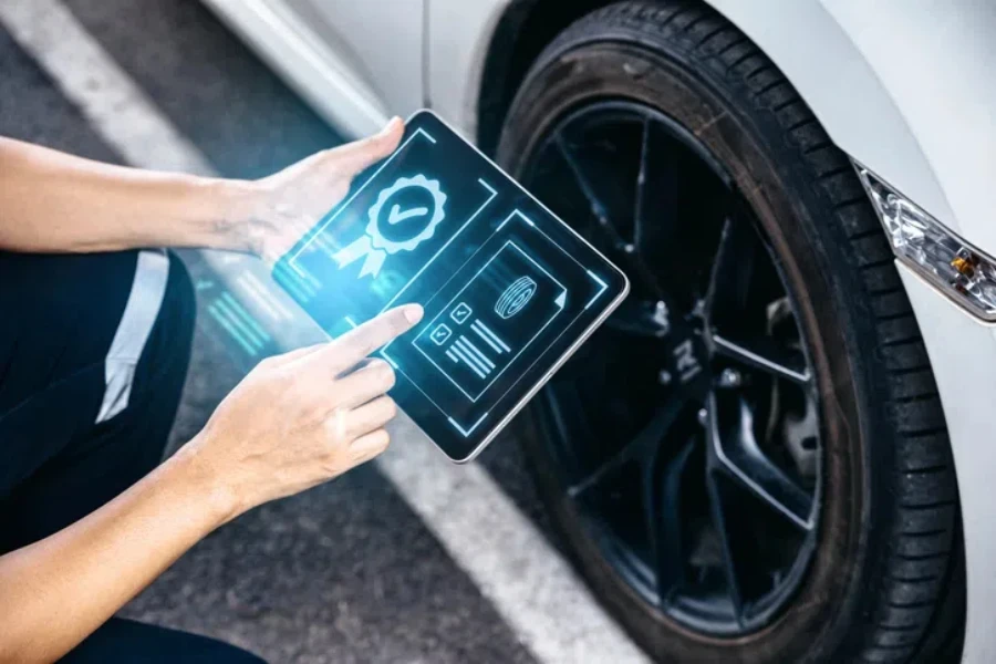 Mechanic technician holding tablet and checking to car tire in auto repair shop garage