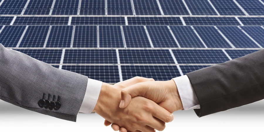 Men shaking hands in front of photovoltaic panels