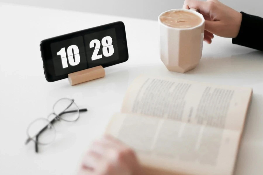 Person Reading a Book with Digital Clock on a Desk