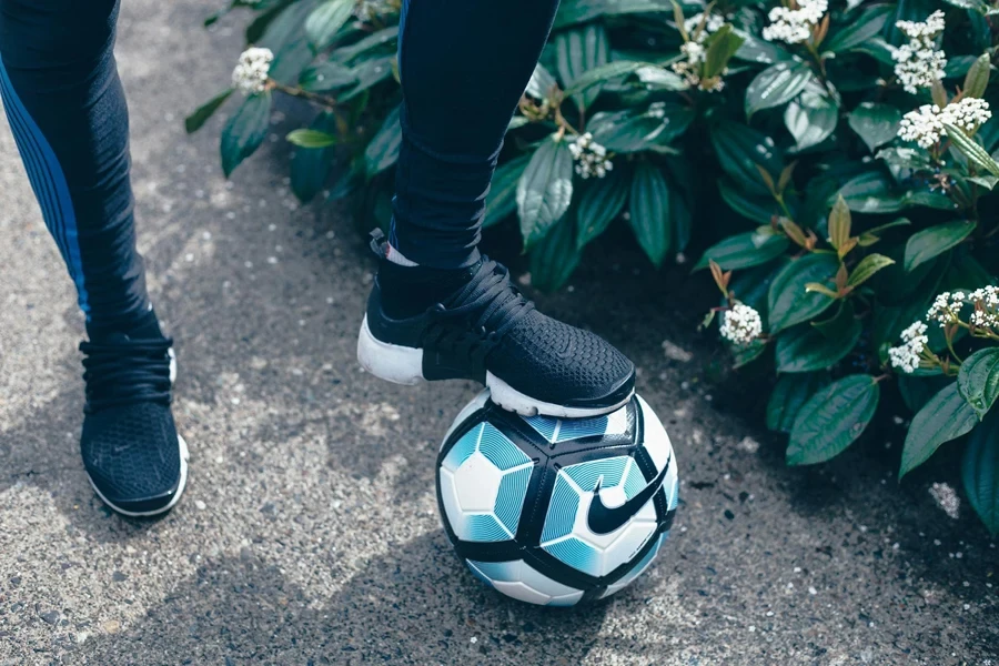 Person in Black Pants and Black and White Nike Soccer Cleats Stepping on Football 