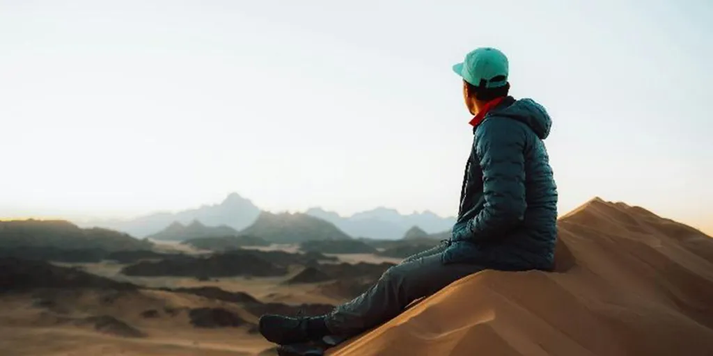 Person sitting on top of sand dune