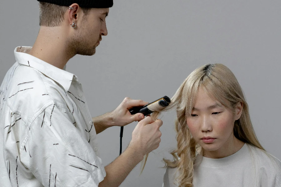 Photo of a Man Using a Curler on a Woman's Hair