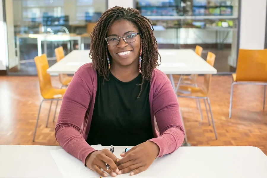 Positive African American female student with braids using smartphone