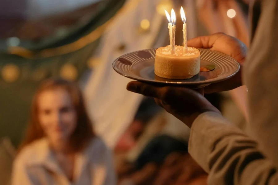 Selective Focus Photo of a Person Holding a Plate with a Birthday Cake