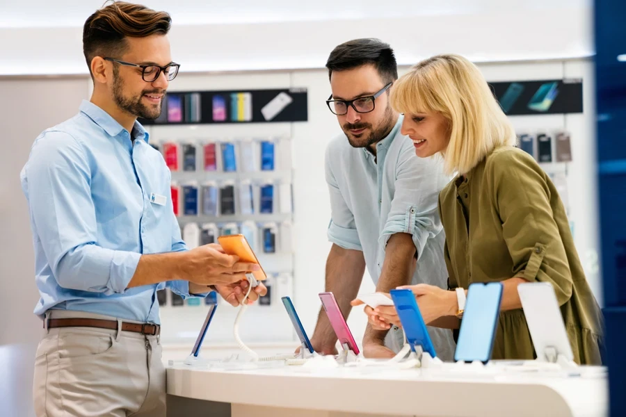 Seller man helping a couple to buy a new digital smart device in a tech store