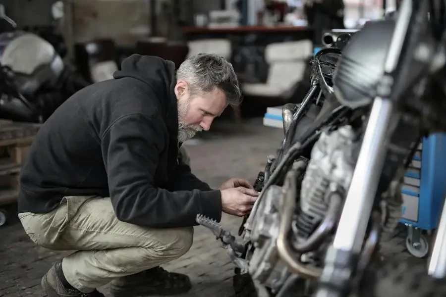 Side view of focused male mechanic in casual wear sitting near motorbike and examining details details in workshop by Andrea Piacquadio