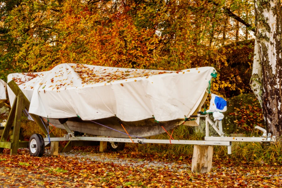 Small recreational boat under a tarp on a trailer in fall