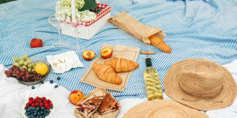 Straw Hats and Flowers Beside Fruits and Bread on Picnic Blanket